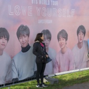 Frau steht vor Plakatwand mit BTS Group Mitgliedern