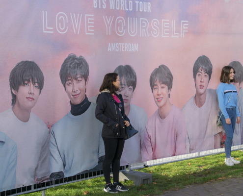 Frau steht vor Plakatwand mit BTS Group Mitgliedern