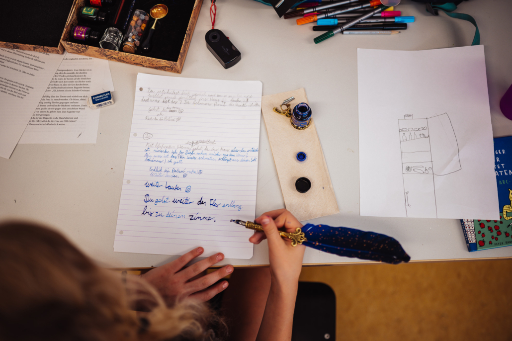 Mit blau gefärbter Feder und blauer Tinte schreibt ein Mädchen auf liniertes Papier.